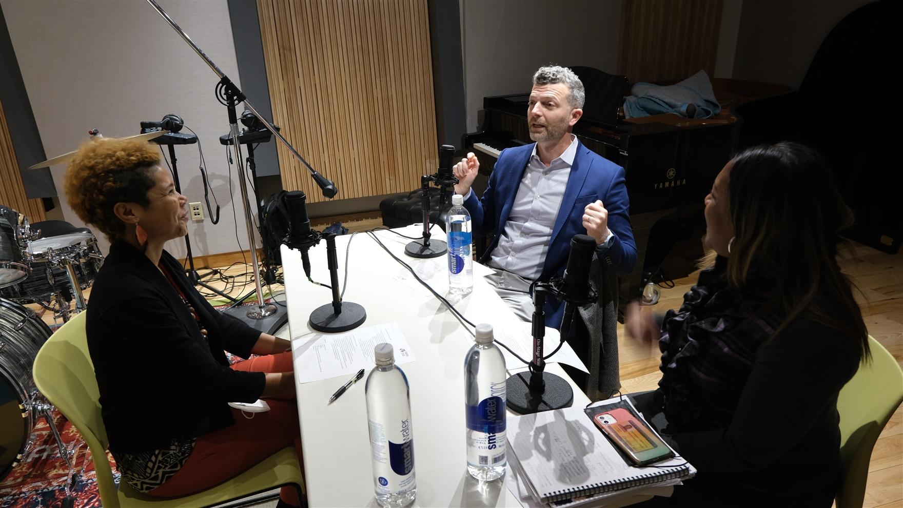 Three people seated at a table to record a podcast.