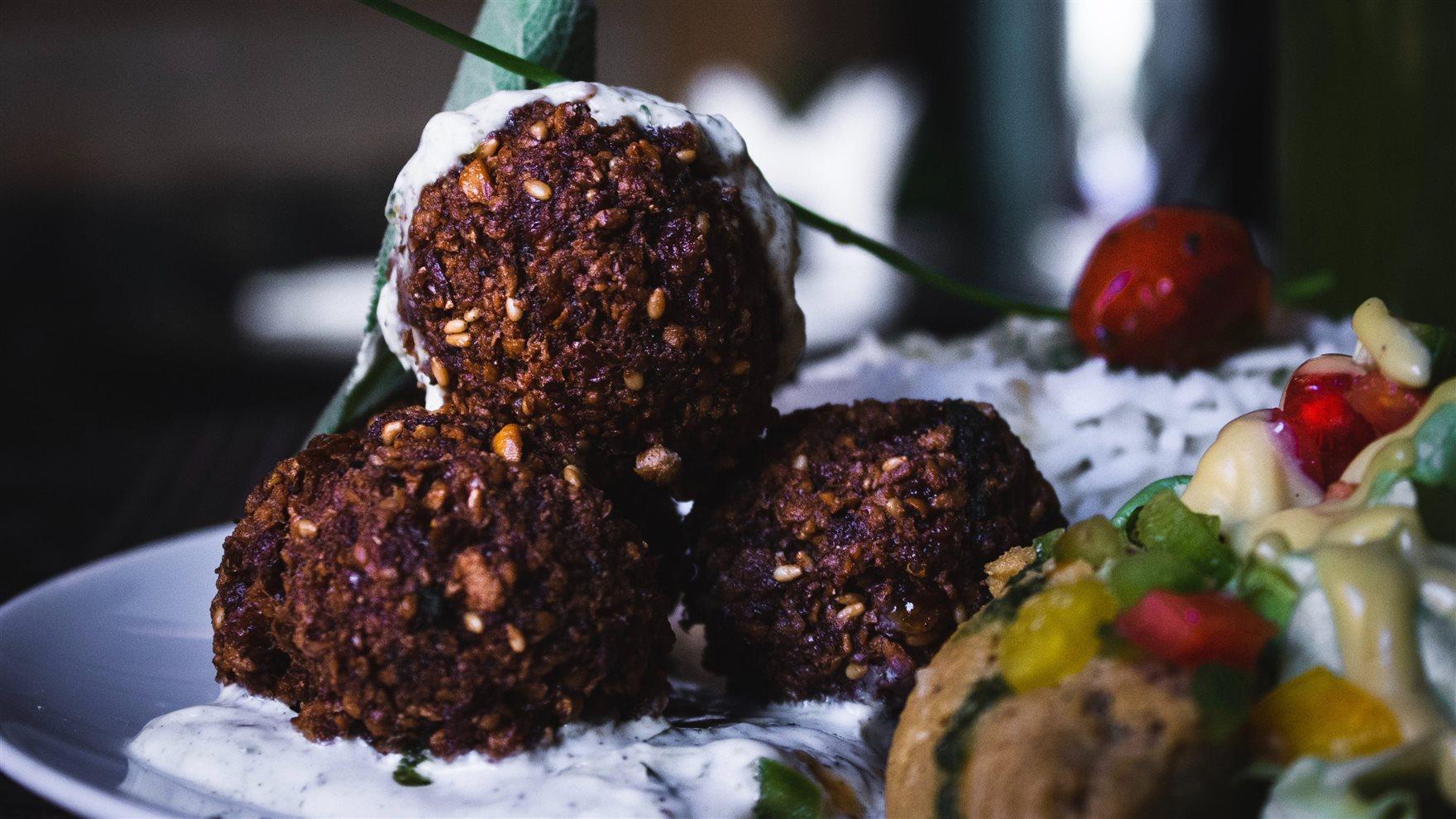 Meatless meatball on a plate with a dip surrounded by vegetables.