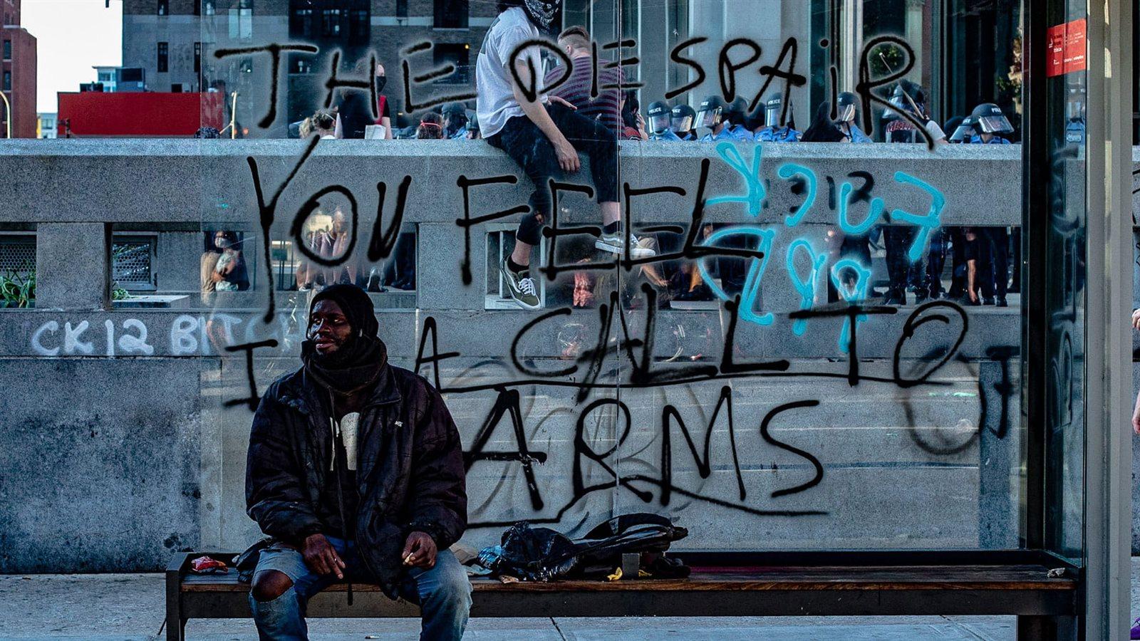 A man sits in a bus terminal spray-painted with the words &quot;The despair you feel is a call to arms.&quot;