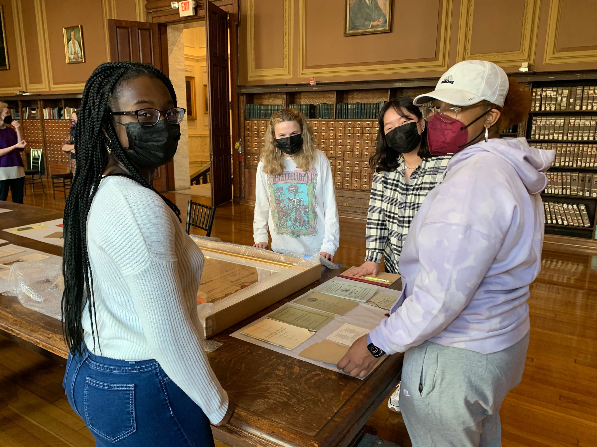Masked students posing on a table with primary source documents at an on-site visit to the museum. Photo courtesy Jacqui Bowman.