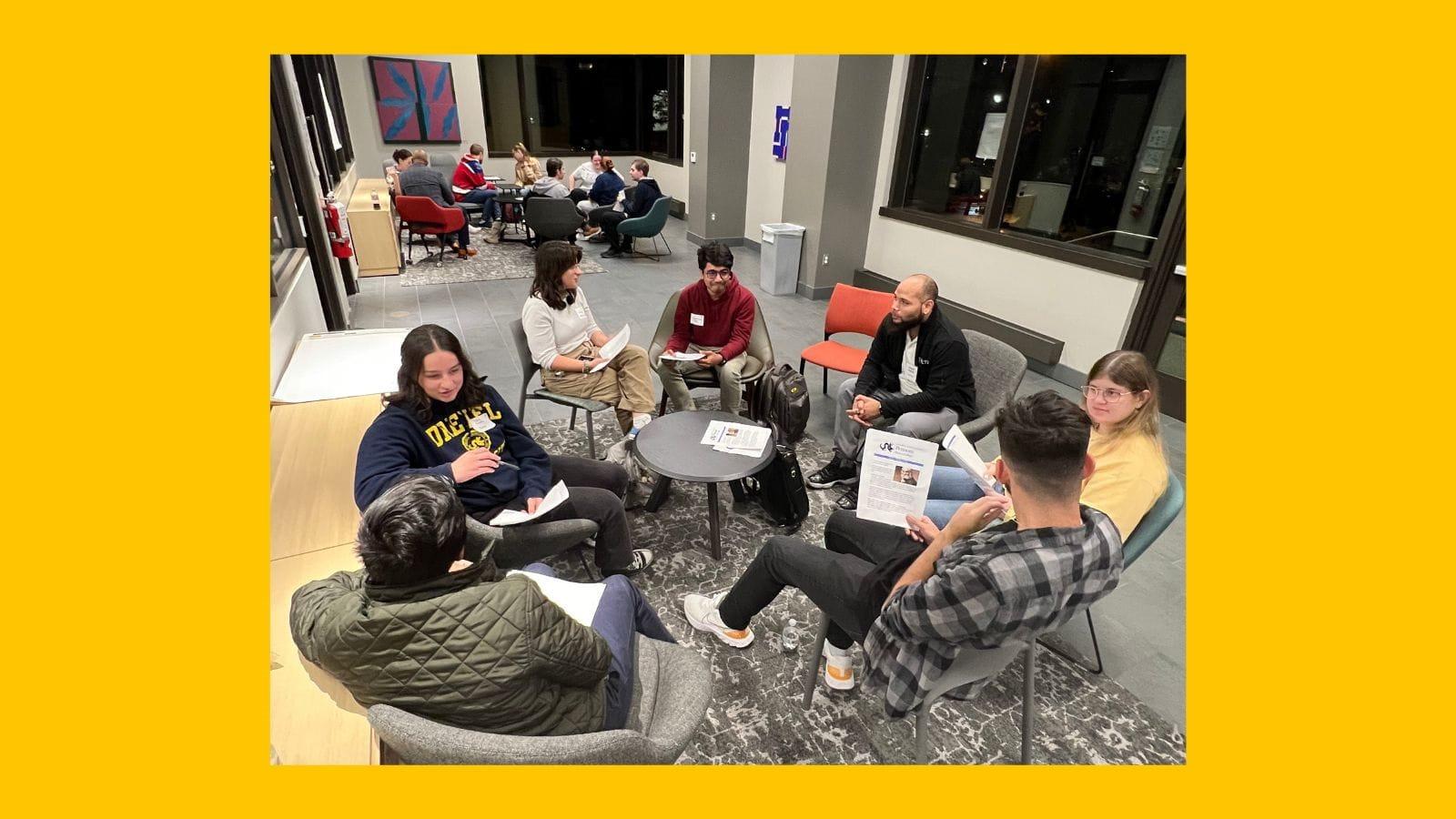 Students sit and discuss Can We Talk prompts in Bentley Hall on a yellow background.