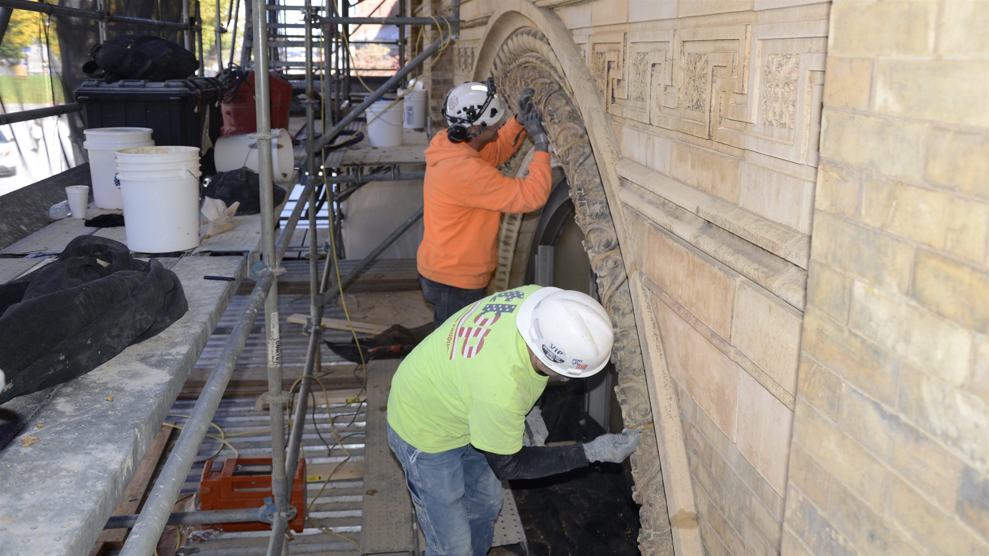 Two construction workers on scaffolding clean terracotta on Main Building.