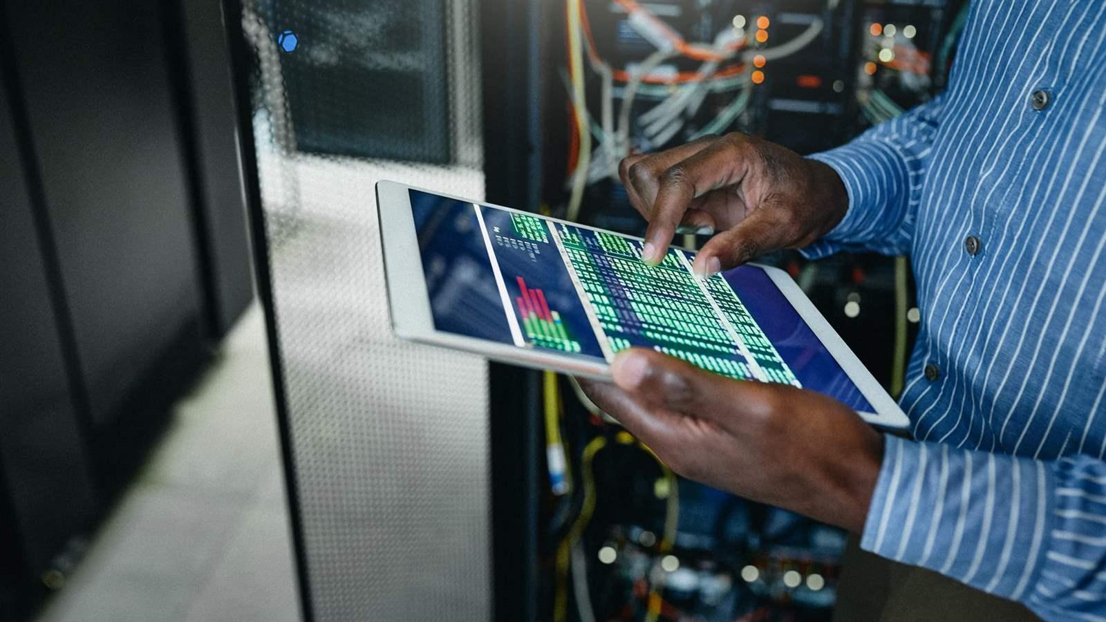 A young man uses a tablet in a server room.