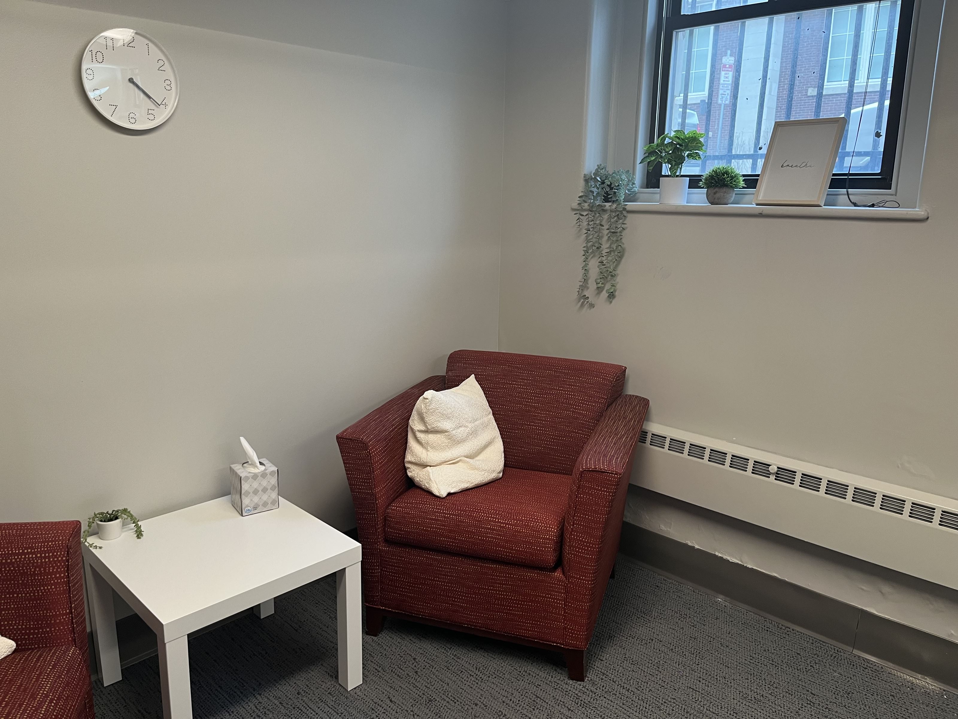 Two red chairs with colorful pillows stationed around a table in a room with minimal decorations and plants.