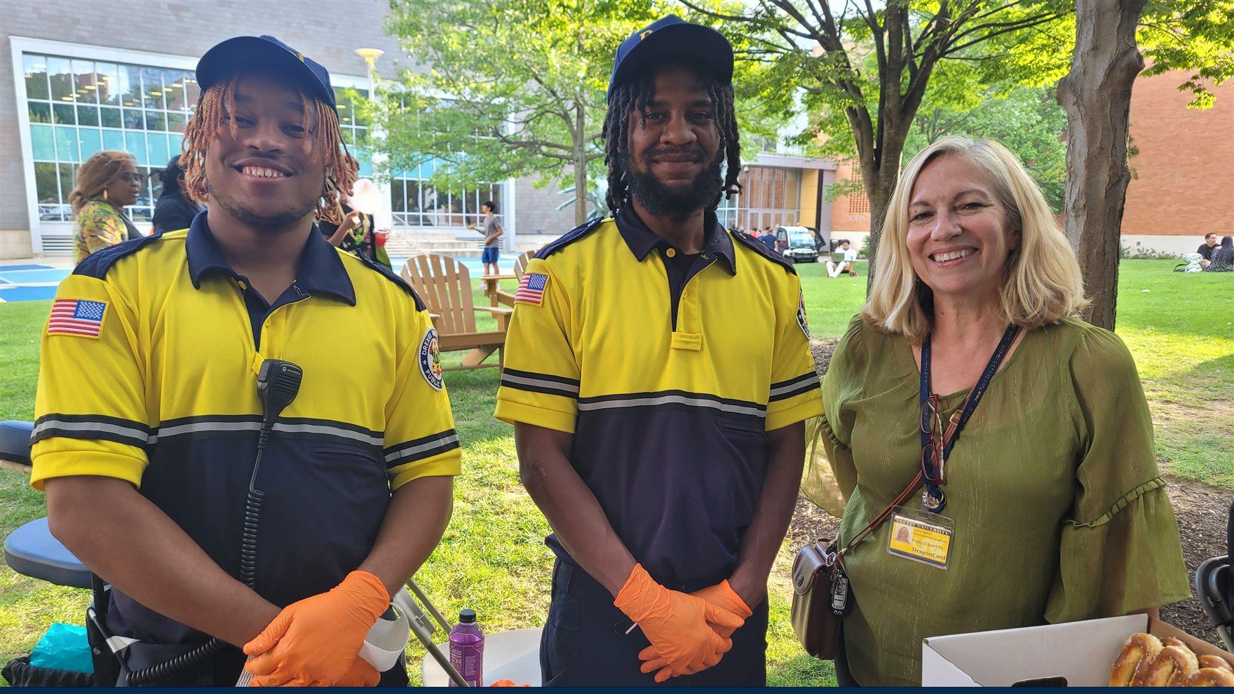 Two public safety officers in uniform and a woman stand at a table. "Public Safety &amp; U" is written on the bottom.
