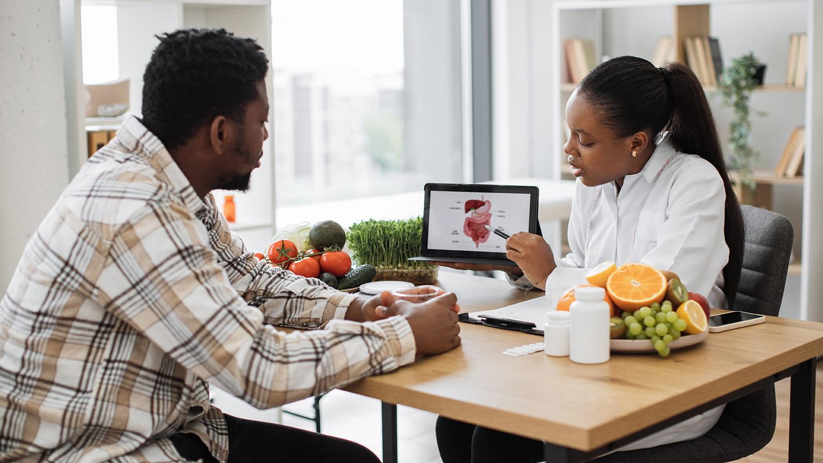 man sitting with woman while she points at a GI tract on a tablet screen