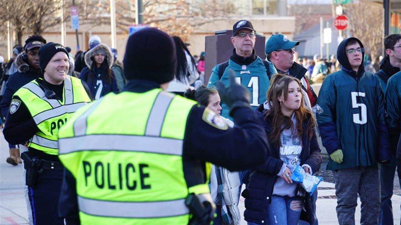 Image of two people wearing fluorescent police vests on Drexel's campus directing foot traffic of people wearing Eagles jerseys and apparel.