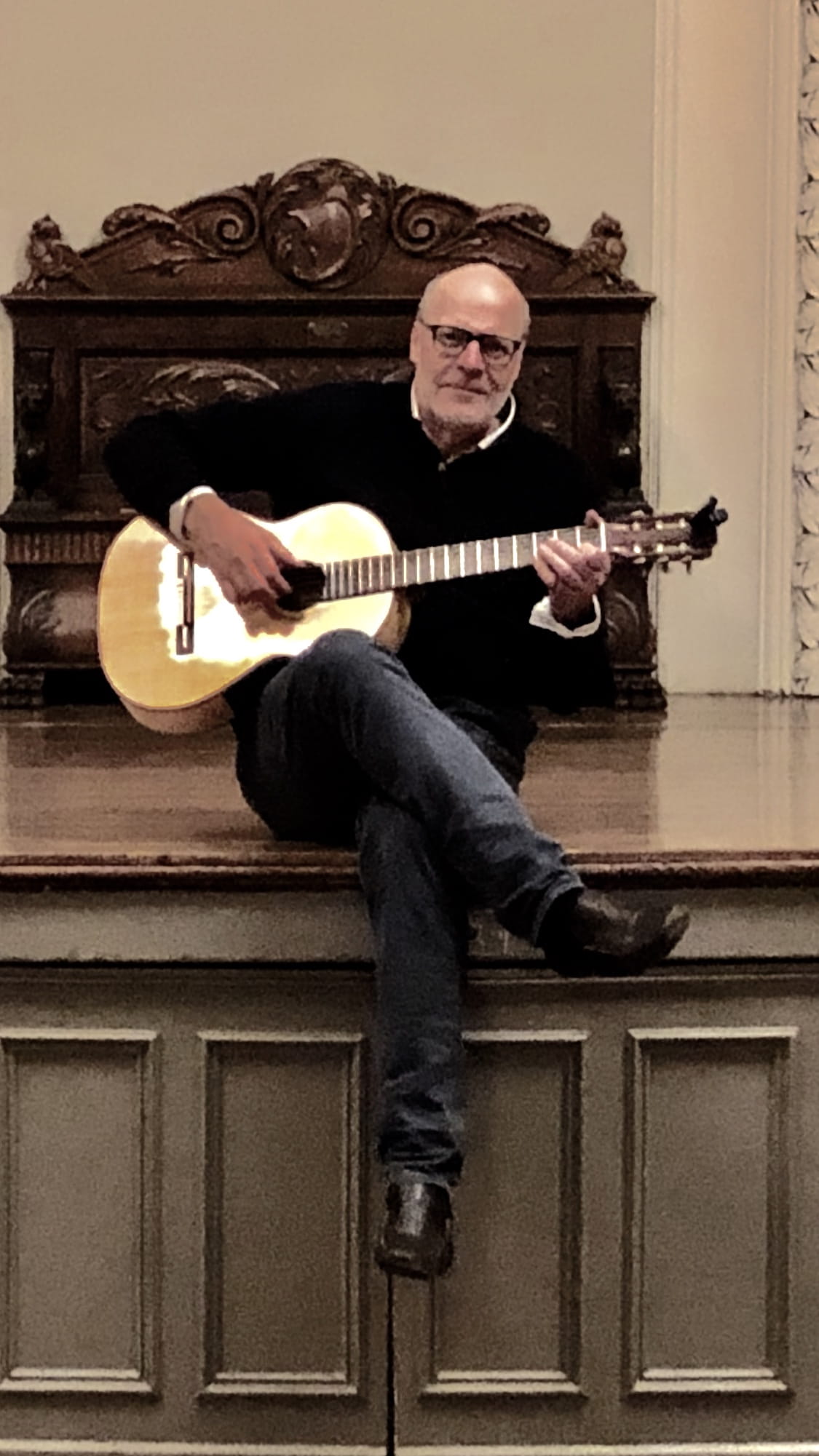 A man sitting on a stage and posing with a classical guitar.