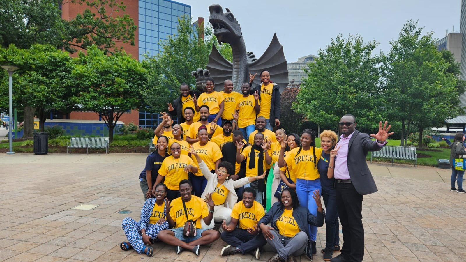 A group of people wearing yellow Drexel shirts crowd around the Mario statue on Drexel&#39;s campus.