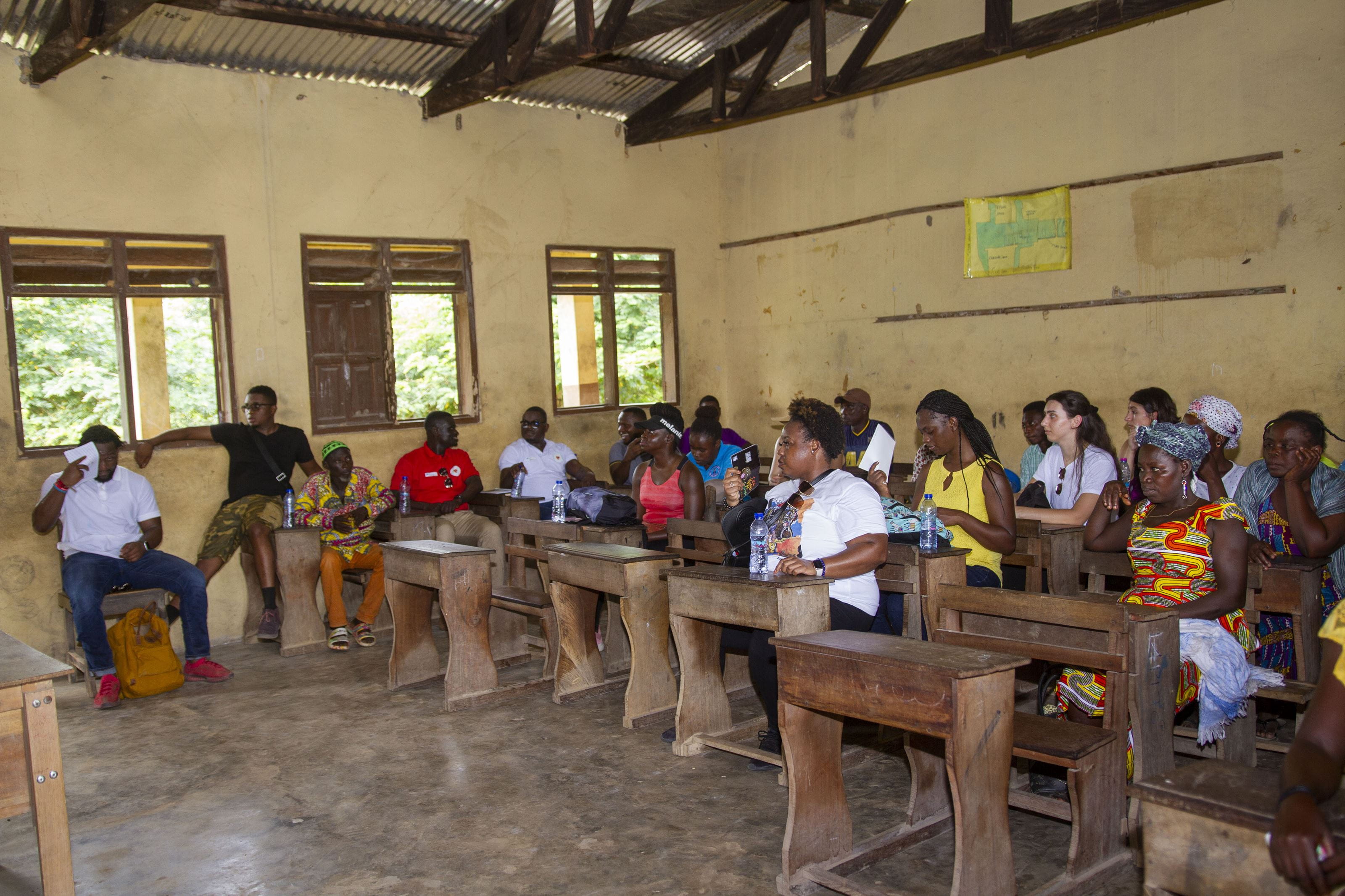 People seated at desks and chairs in a room with windows. 