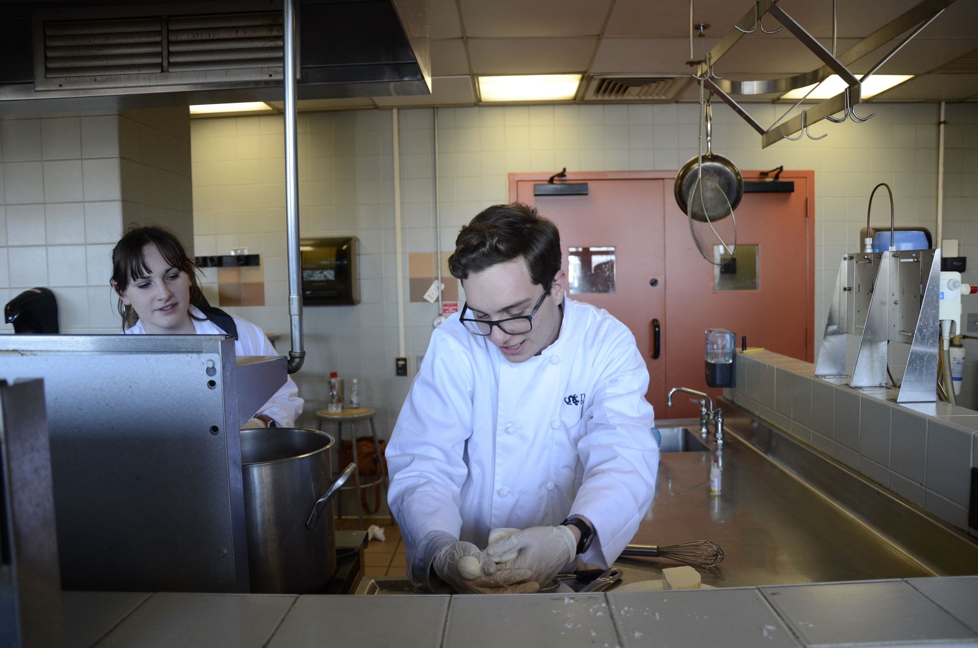 A female student watches as a male student shapes the mozzarella into a smaller ball.