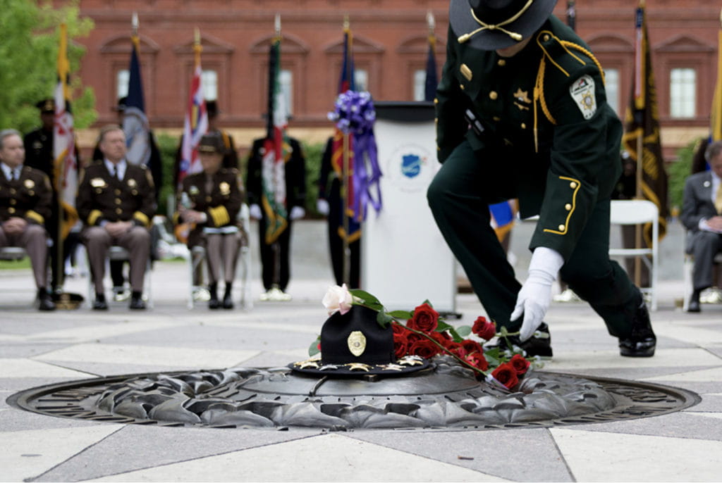 Image of an officer placing flowers over a memorial on the ground as people watch in the background.