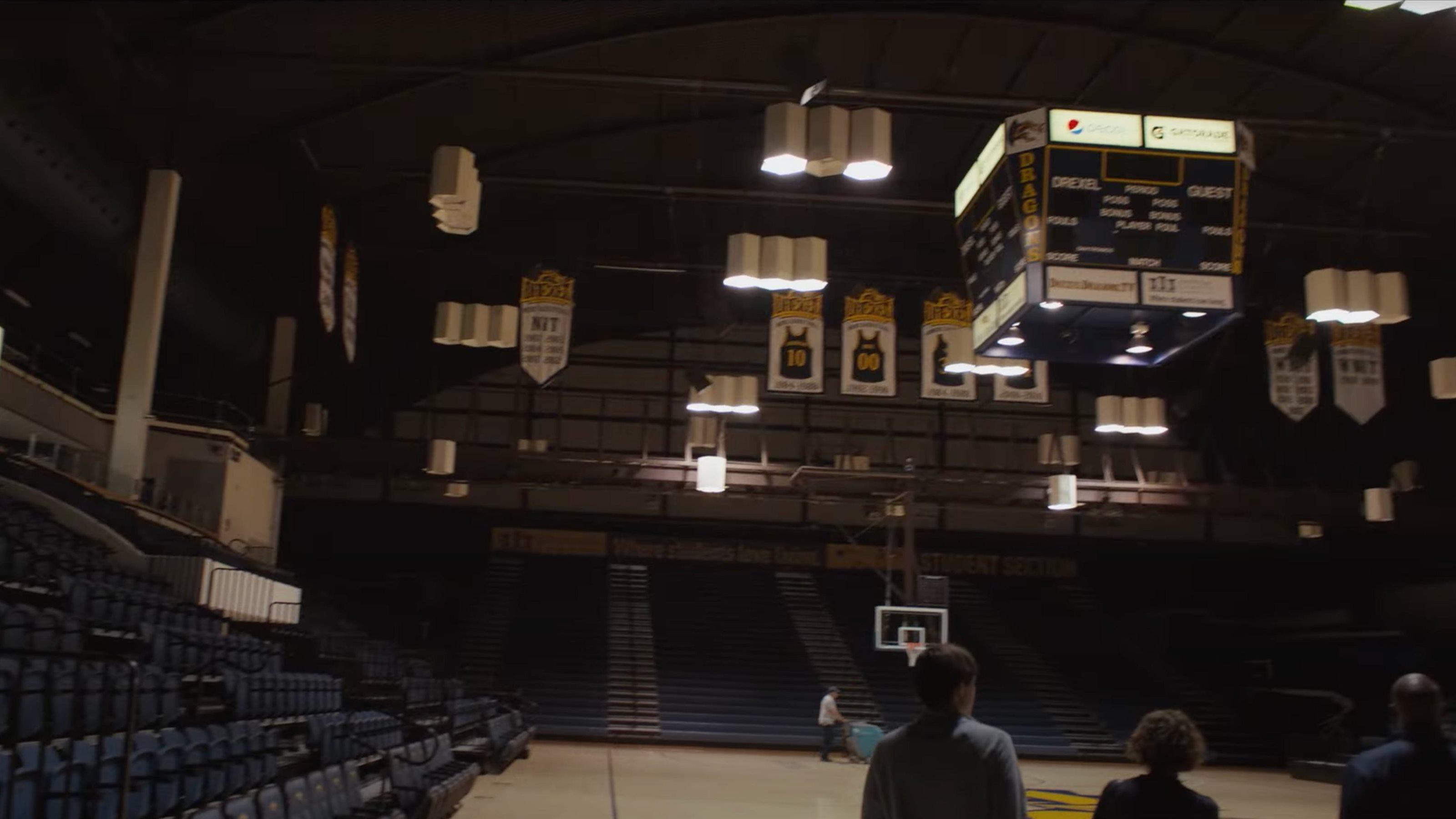 Image of hanging Drexel jerseys and the scoreboard over a basketball court people are walking on near the stands.