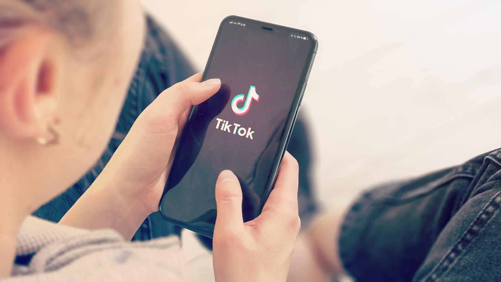 women using a phone displaying the TikTok logo