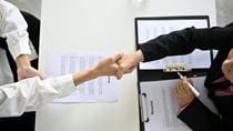A person interviewing for a job shakes hands with an interviewer.