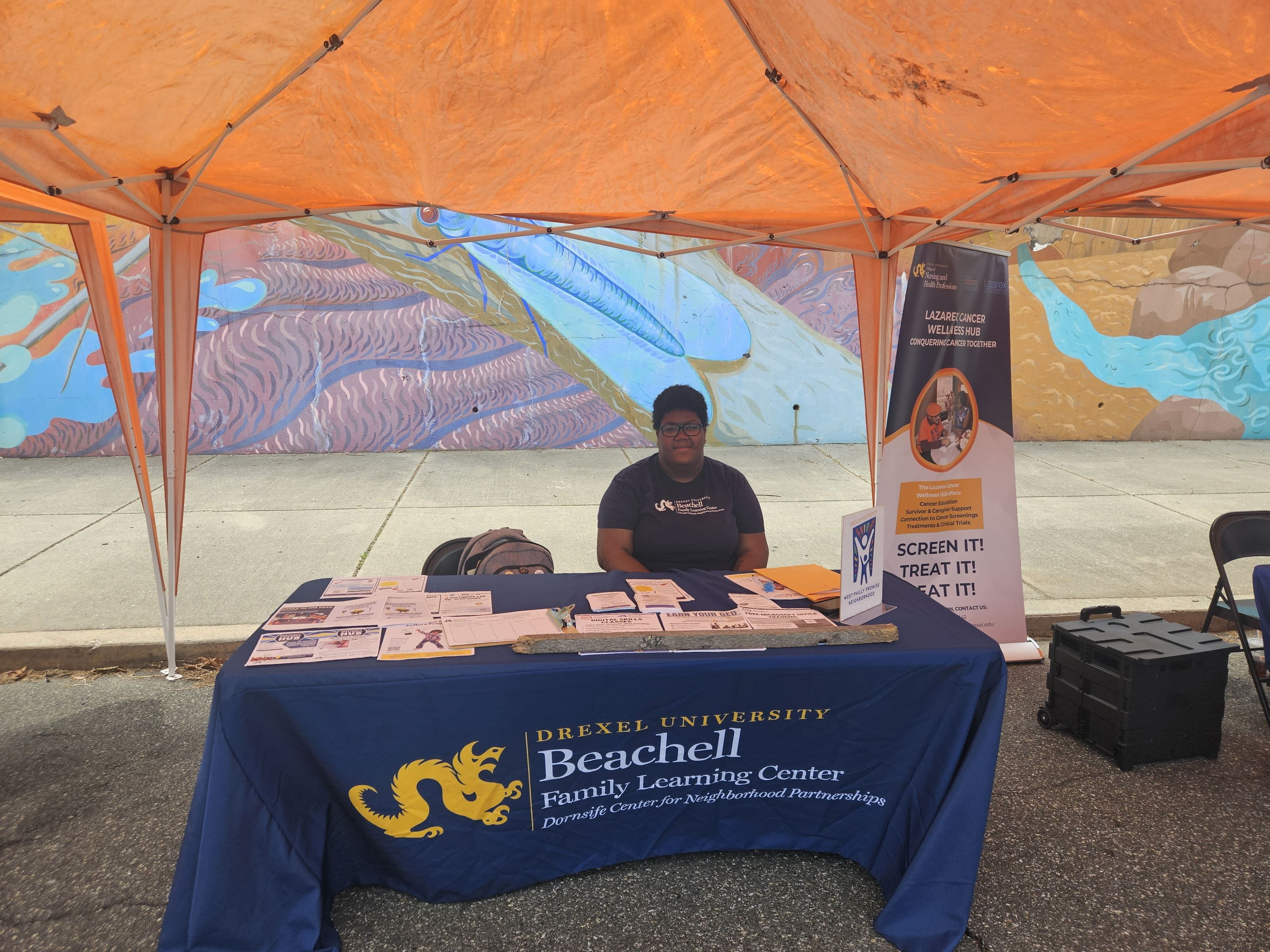 A female student sits behind a table reading "Drexel University Beachell Learning Center."