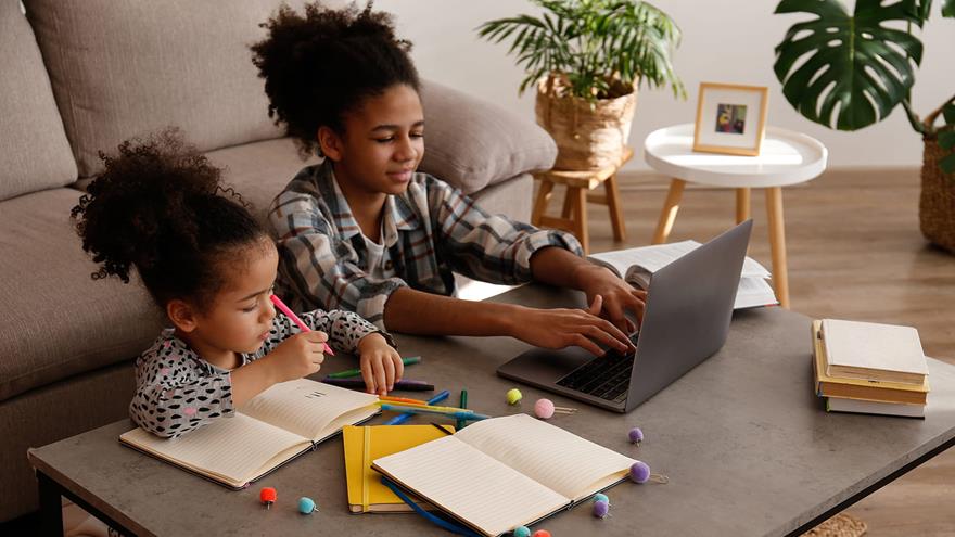 teen girl playing on laptop next to younger girl coloring