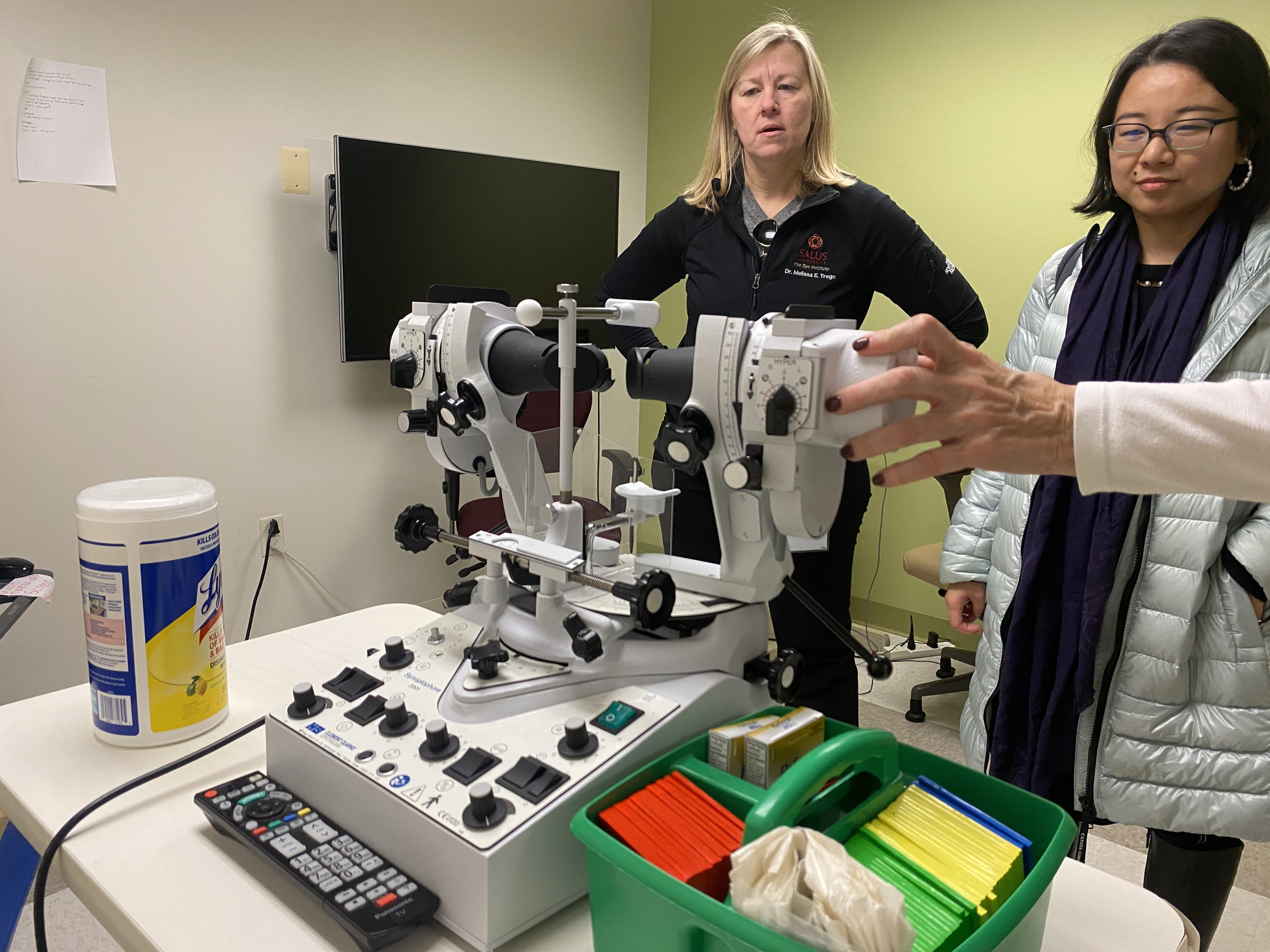 Melissa Trego, left, and June He photographed observing a synoptophore (an ophthalmic device that eye care professionals use to assess and treat binocular vision disorders and eye muscle imbalances) during a tour of The Eye Institute’s spaces in November 2023. Photo credit: Khue Dao. 