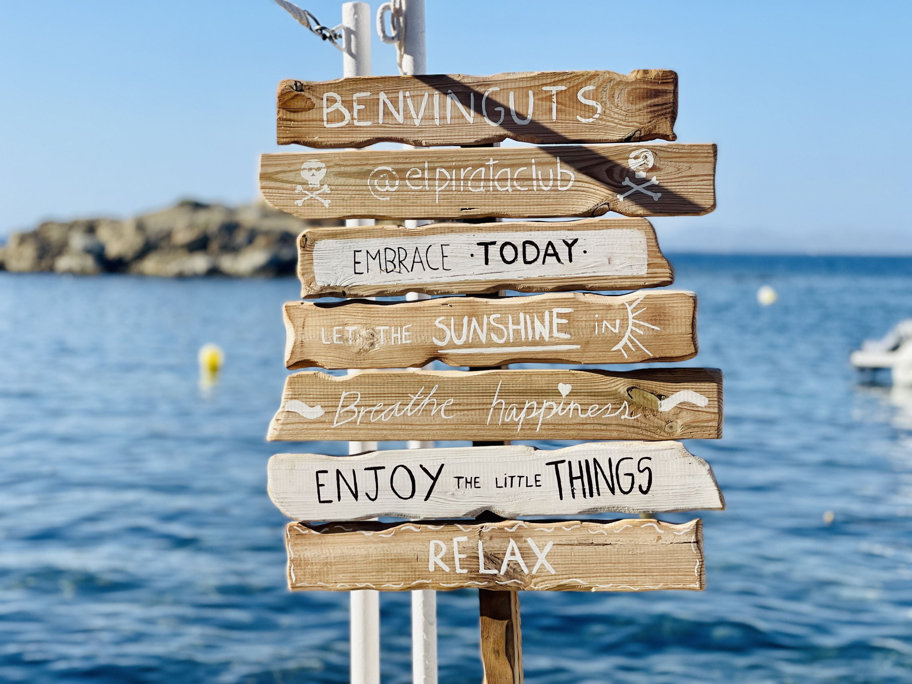 A stack of wooden signs with sayings on a beach.