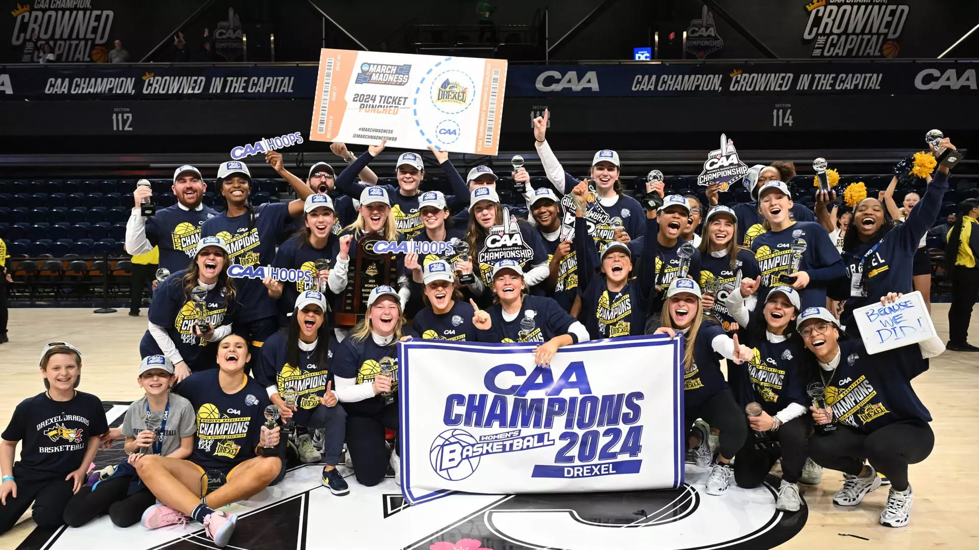Drexel's 2024 women's basketball team sitting on the court with "CAA Champions" signs.