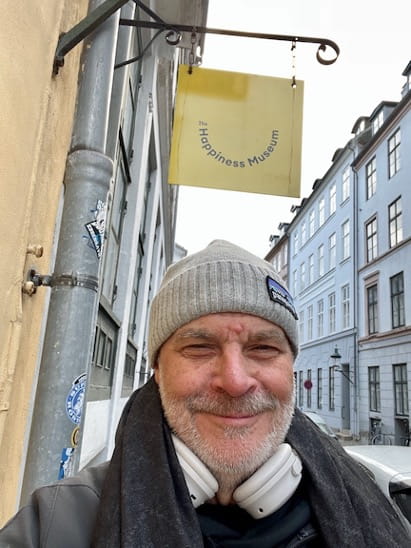 A man in a hat standing under the sign for the World Happiness Museum.