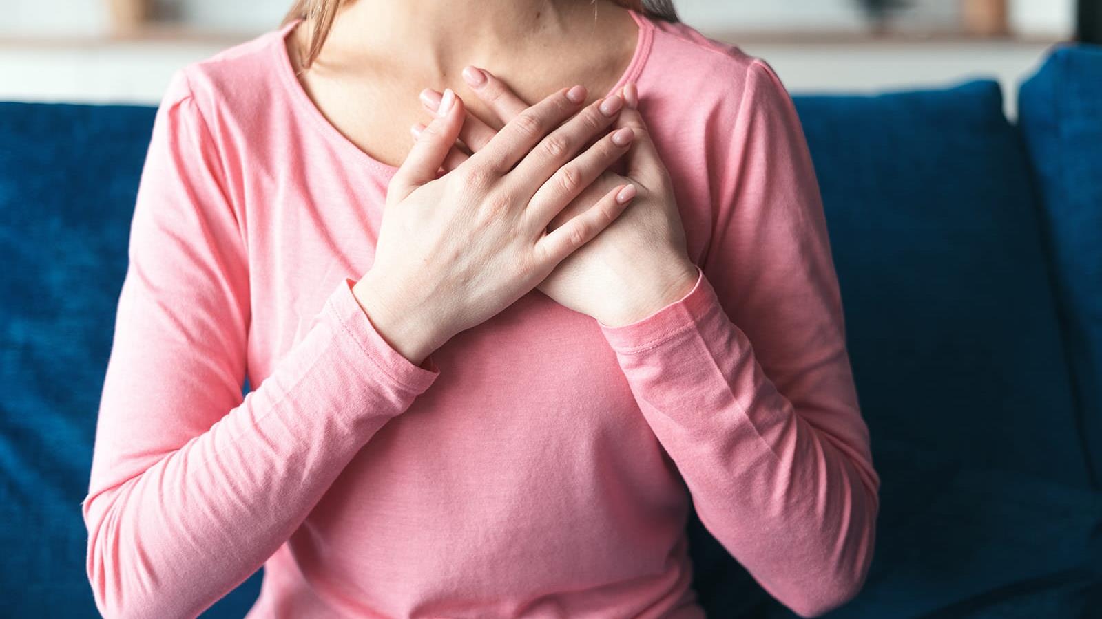 woman in pink shirt with her hands resting on her chest over her heart