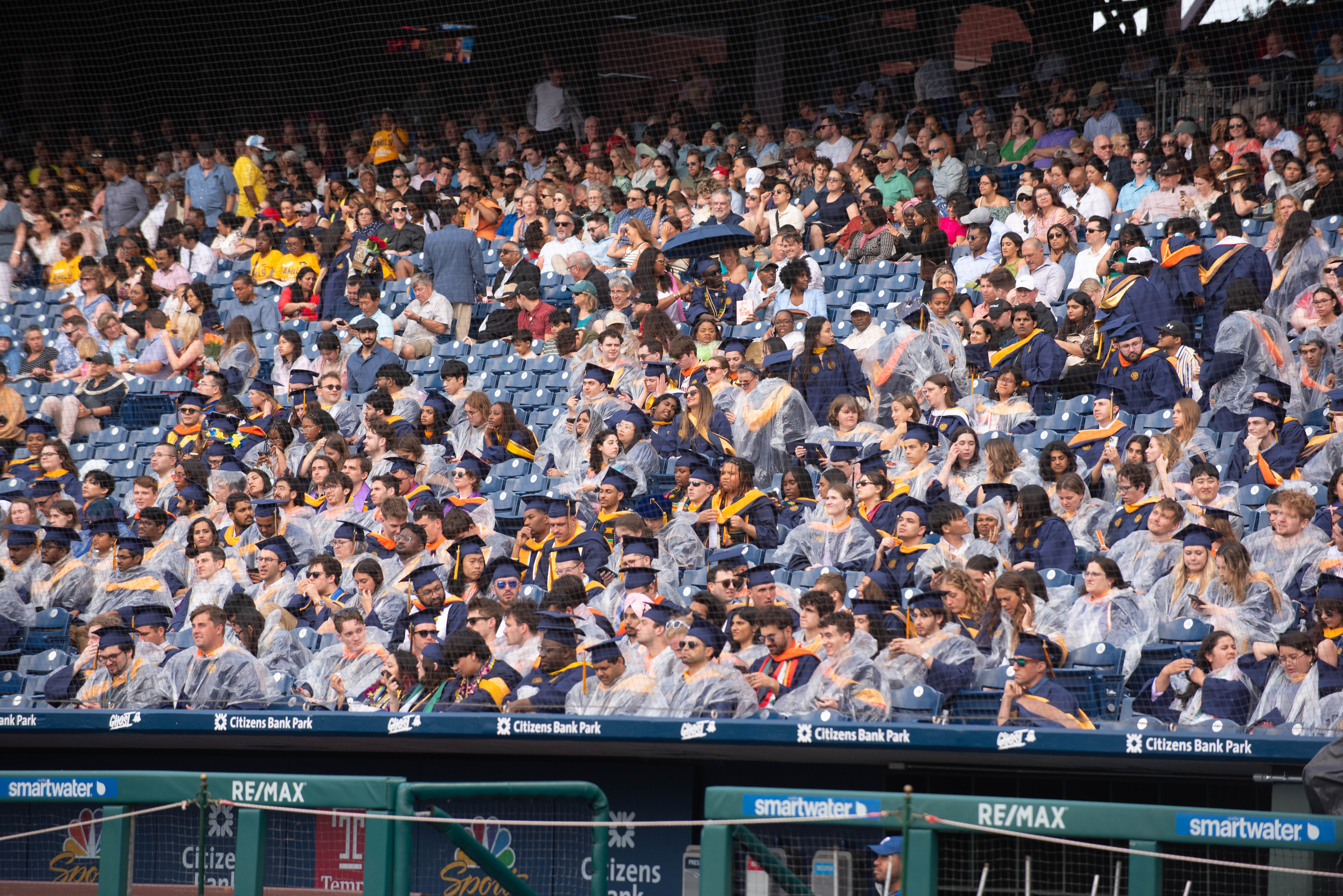 Students in Commencement regalia, some with ponchos and umbrellas, in the stands of Citizens Bank Park for Drexel's 2024 Commencement.