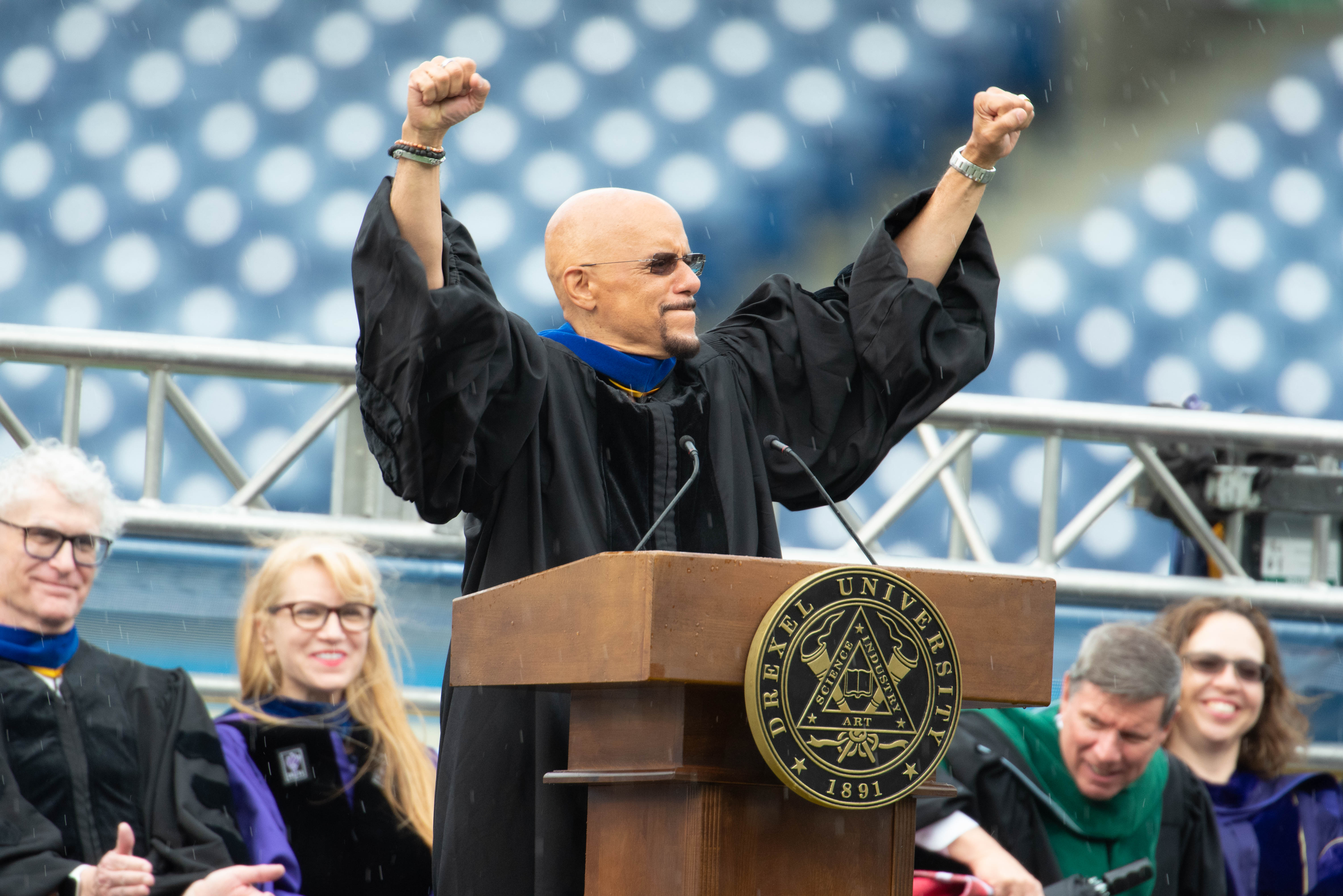 Pennsylvania State Sen. Vincent J. Hughes with arms raised while speaking at the podium at Drexel's 2024 Commencement.