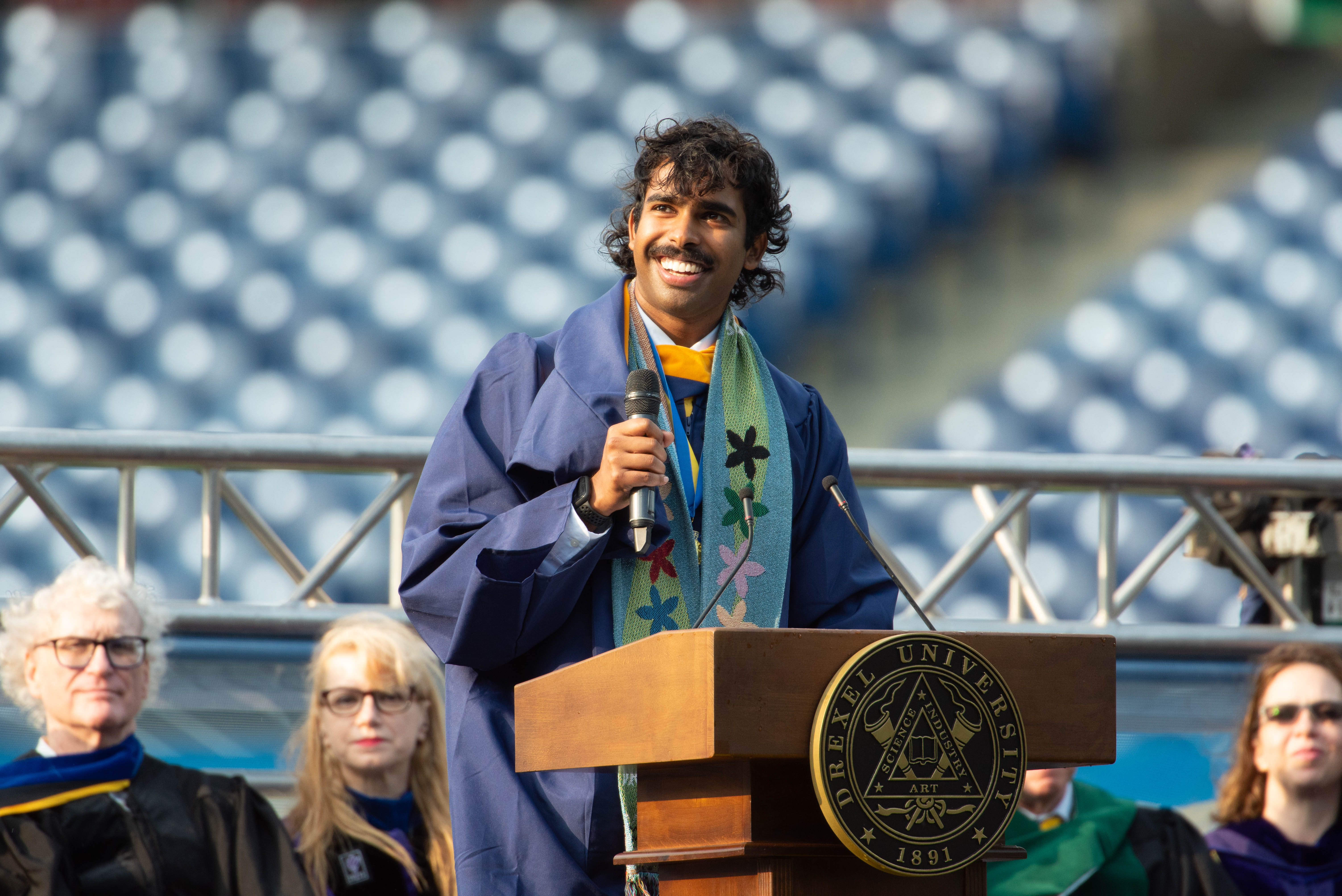 Vivek Babu speaking into a microphone at Drexel University's 2024 Commencement ceremony.