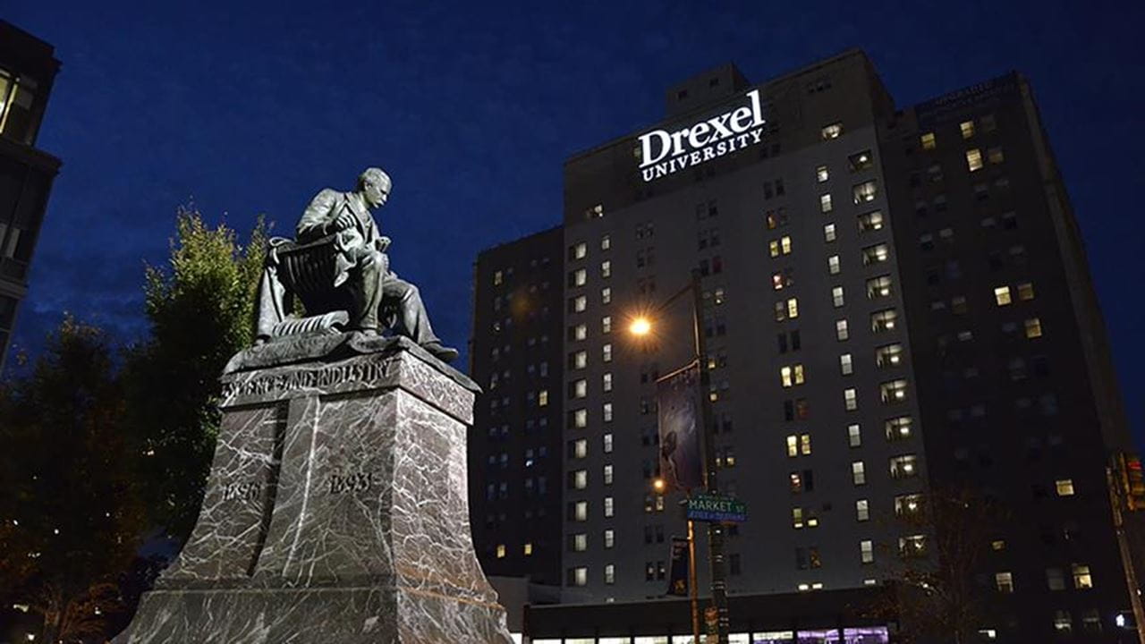 AJ Drexel statue at night under a building with DREXEL on the front