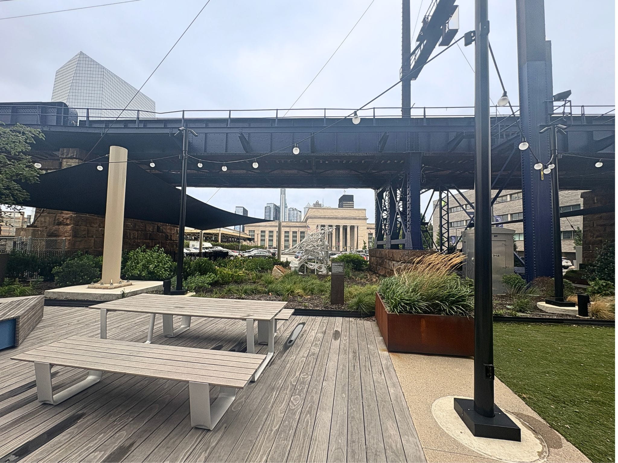 Table and chairs outside by a white sculpture with 30th Street Station in the background.