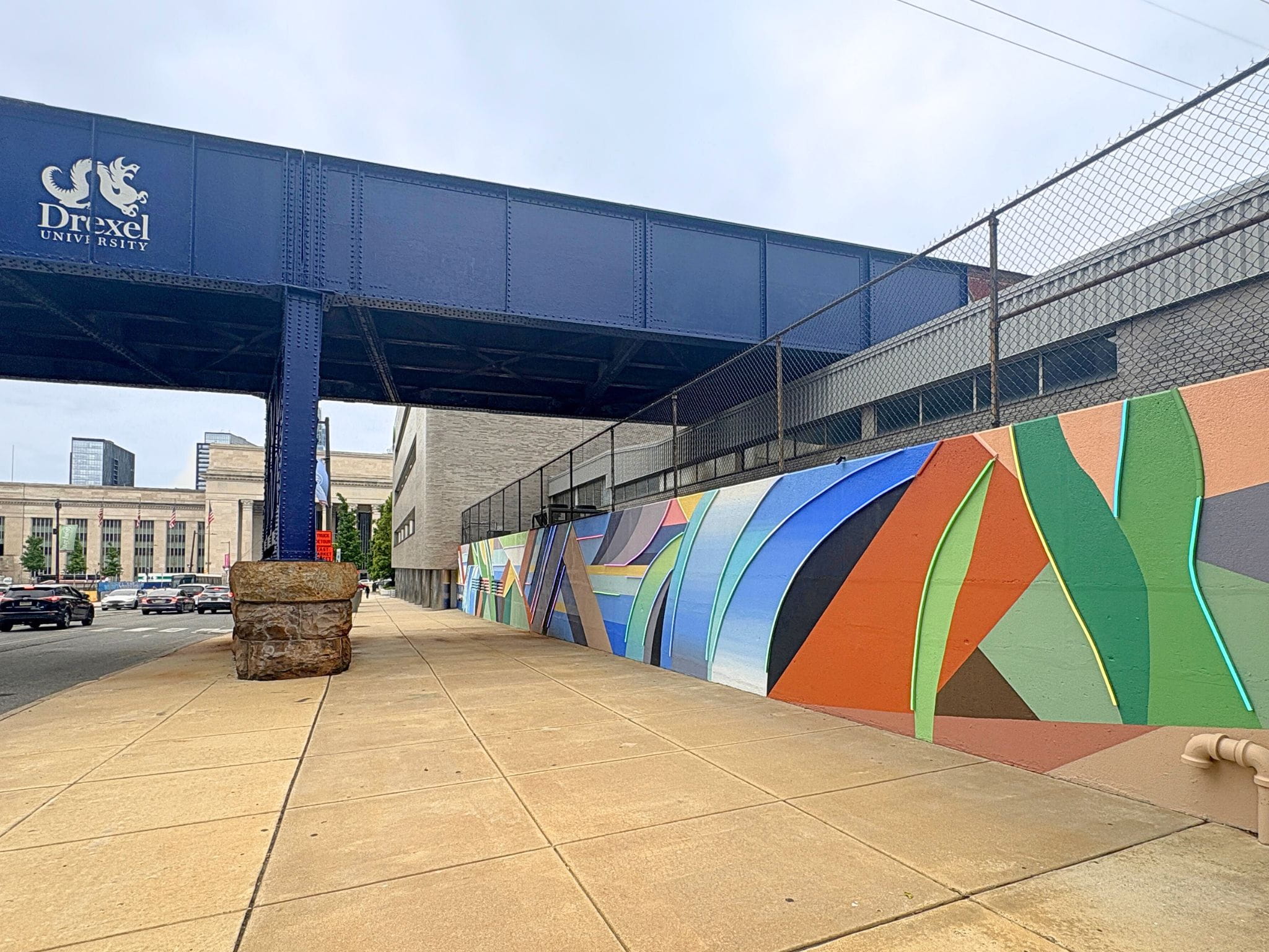 A row of colored paint on a wall under an elevated train track