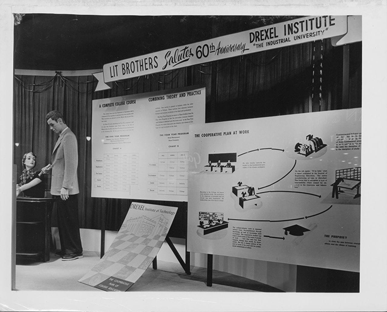 Photo of a window display with two mannequins and a sign reading "Lit Brothers Salutes the 60th Anniversary of the Drexel Institute of Techniology."