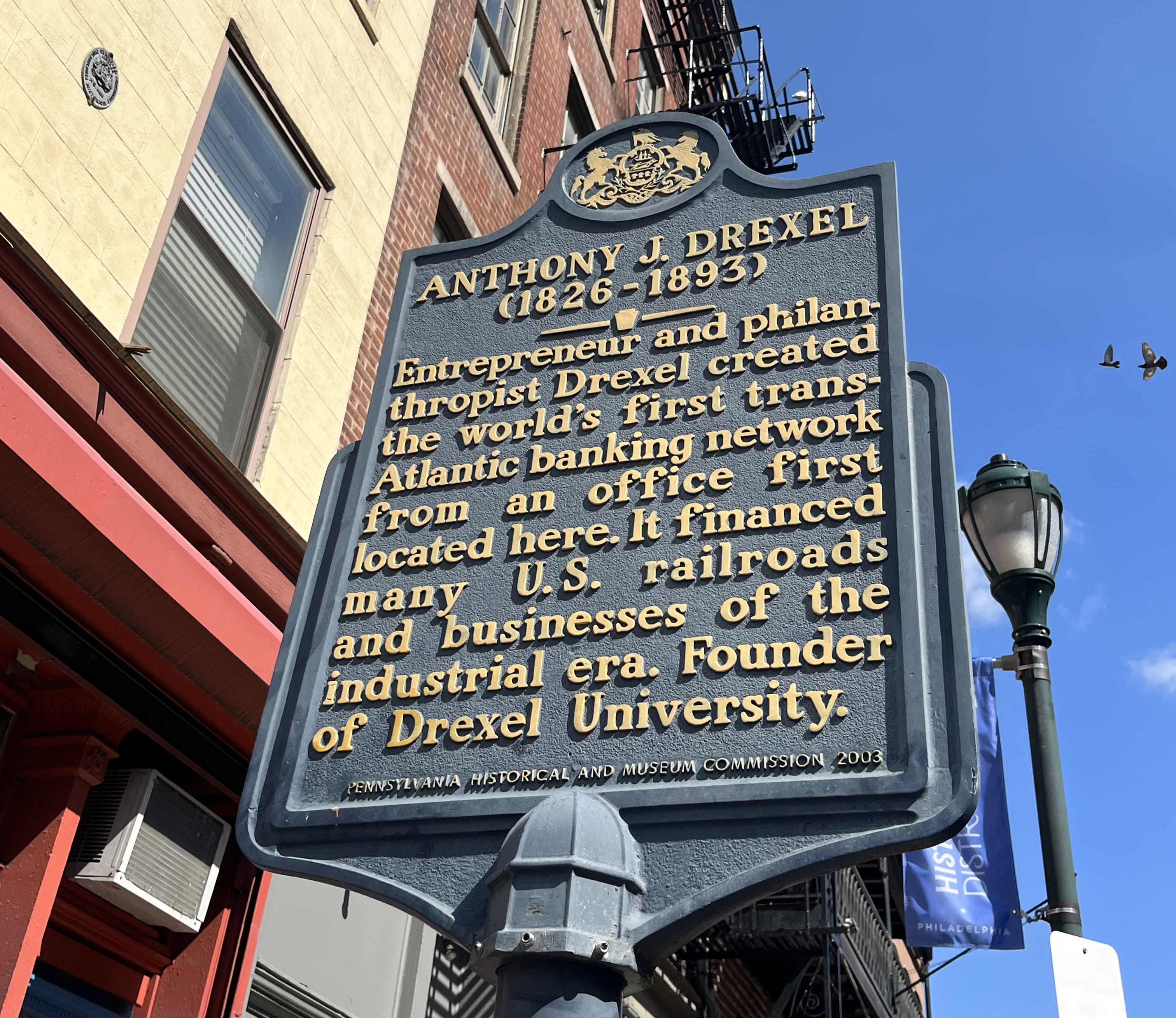The historical marker honoring Anthony J. Drexel that the Pennsylvania Historical and Museum Commission placed in front of the original 1838 location of Drexel & Co. (48 South Third St.) in 2003. This picture was taken in August of 2023 — note the red of the building that has since been painted navy.