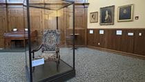 A view of a historical chair in a glass case in front of Drexel portraits.