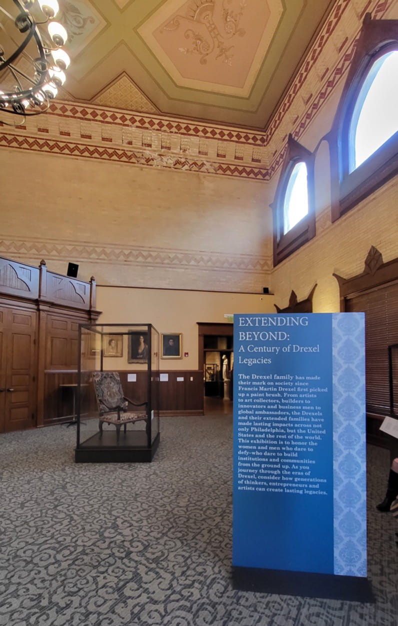 The right side of the room showcases the standing sign introducing the exhibition, with an early 18th century chair displayed behind it, also donated by Philip Syng Physick Fell. On the wall are portraits (from left to right) of Pauline Munn Doyle, her mother Mary Astor Paul Allez, and Alice Troth Drexel. Photo by Gina Monahan.