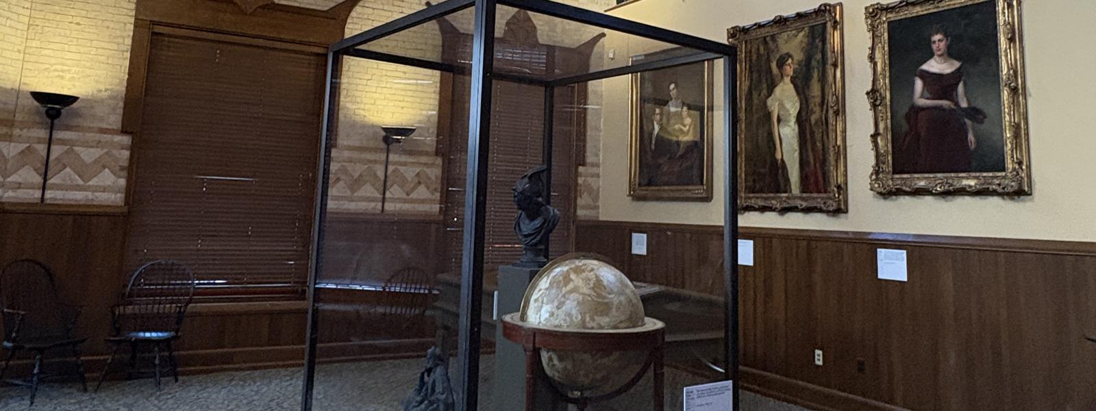 A globe stationed in front of portraits on a wall.
