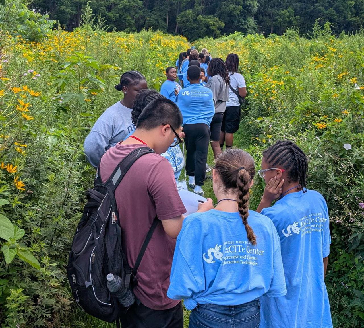 Children in light blue ExCITe Center shirts outside in a grassy area.