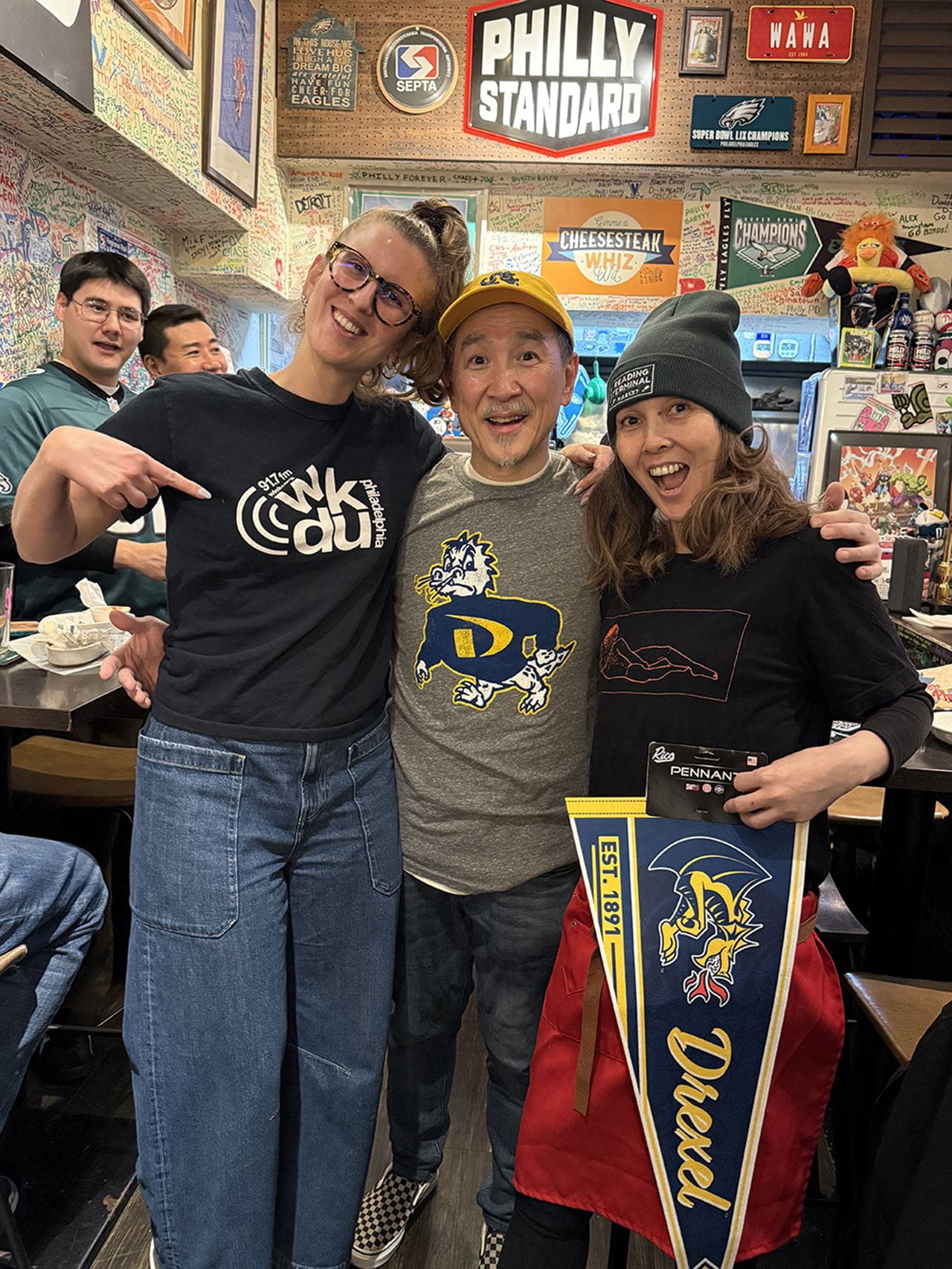 During her visit to Nihonbashi Philly in December, Monika Julien, who is also a Drexel alumna, wore a T-shirt for WKDU, Drexel’s independent studio radio statio. The Chujos have the “Drexel swag” she brought from campus: Kosuke, center, is wearing the Drexel hat and shirt, and Tomomi is holding the Drexel pennant. Photo courtesy Monika Julien. 