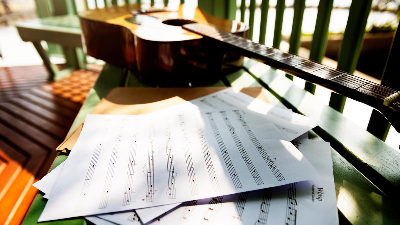 blank music sheets scattered next to an acoustic guitar