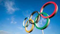  A large set of Olympic rings shines in bright sunlight against blue sky.