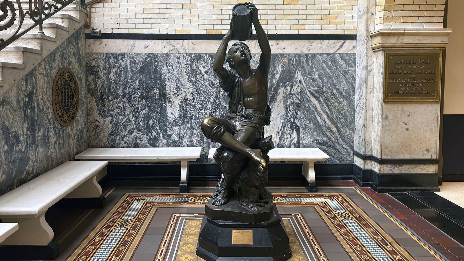 "The Water Boy" statue showing a boy pouring water from a jug while sitting down with his legs crossed.