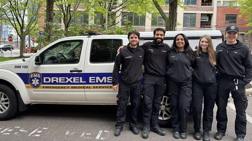 Five student EMS workers in front of a EMS automobile.