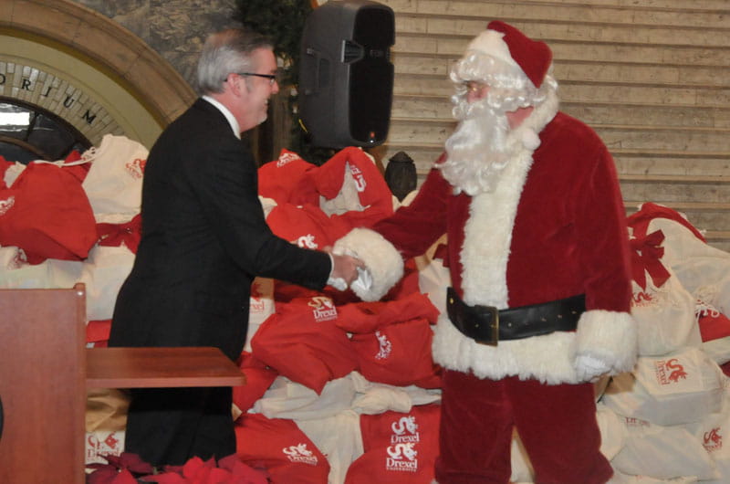 Drexel President John A. Fry shakes hands with Santa Claus at annual toy drive distribution ceremony.