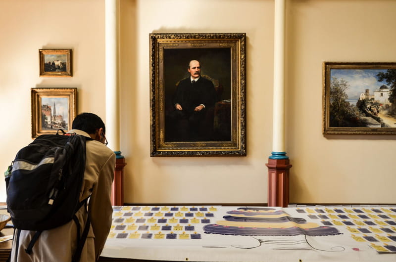 A student writing out his wishes for his time at Drexel on a banner decorated with cakes before a portrait of the University's founder, Anthony J. Drexel. Photo by Ola Baldych.
