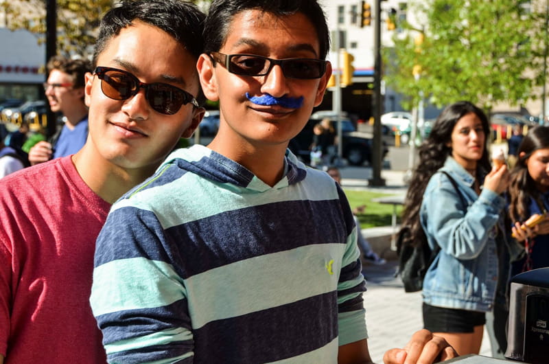 A pair of students waiting for ice cream, one taking advantage of the mustaches made available to students. Photo by Ola Baldych.
