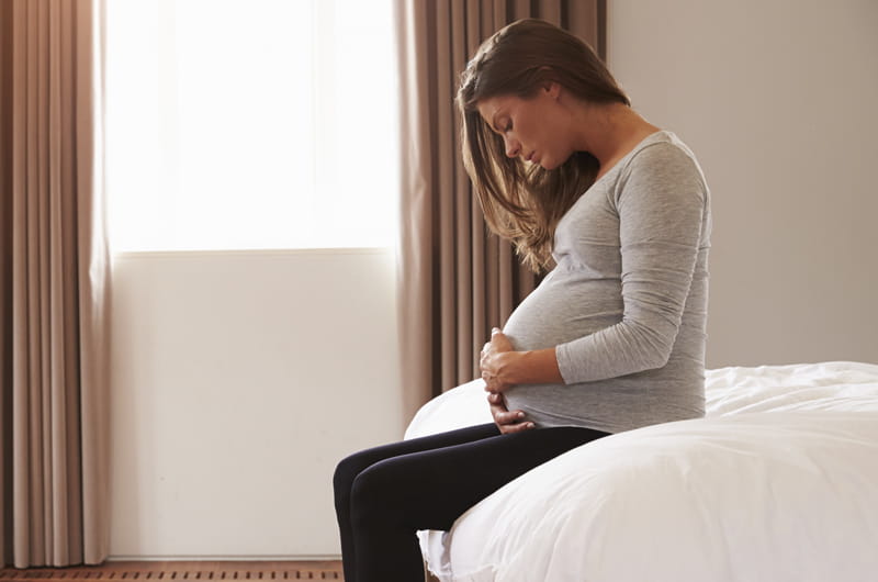 Pregnant woman holding stomach while on bed.