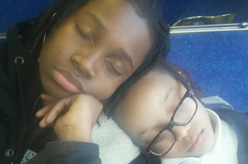 A photo of two boys with their heads together sleeping. Taken by Angela S. of the Philadelphia Witnesses to Hunger, she said, "To get a good education, my sons have to take two buses and a train through the 'hood to get to school. They fight all day, but here they were tired, cold, and supporting each other just trying to get home safe.”