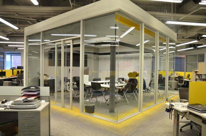 The lab's conference room is surrounded by glass walls in the middle of the student workstations.