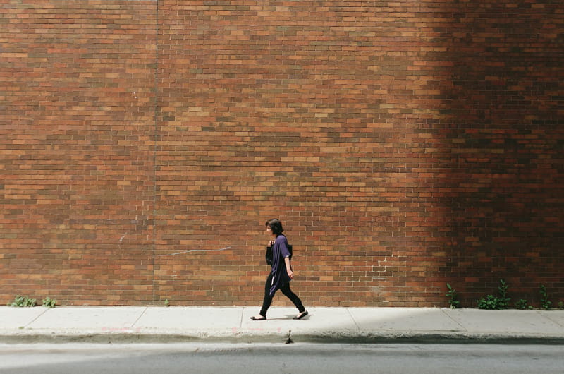 A woman walking on a sidewalk in front of a brick wall.